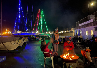 People around a fire with Boats decorated with Christmas Lights