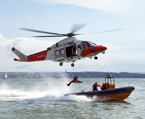 An image of a helicopter hovering above a RIB on the water. A person is being winched from the RIB into the helicopter.