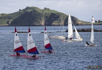 Mixed dinghies in a busy coastal scene with islands and a lighthouse in the distance