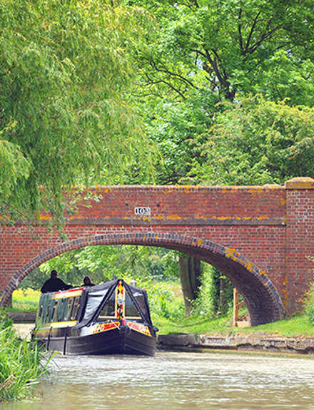 NARROWBOATERS  TRAVELLING UNDER A CANAL BRIDGE ON BARGE RE BRITISH CANAL