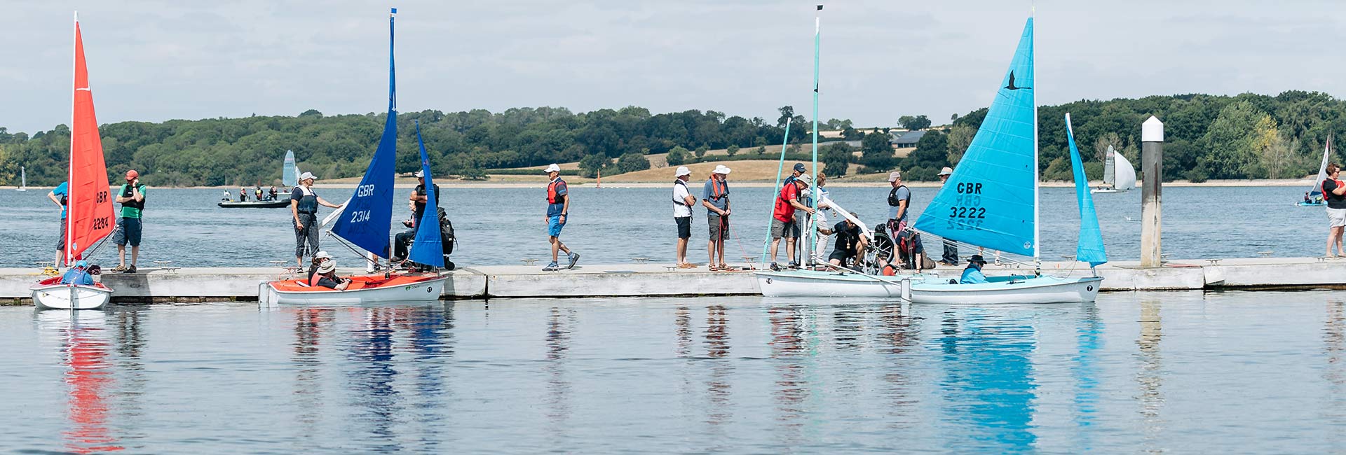 wide shot of people being helped into dinghies by other people at a dock on a lake
