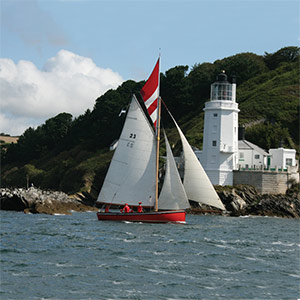 a small sailing boat off the south west coast next to a light house