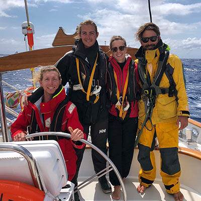posed shot of 4 sailor all wearing lifejackets on a large yacht out on the windy ocean