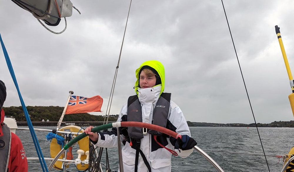 Ellia steering a large wheel on a sailing yacht