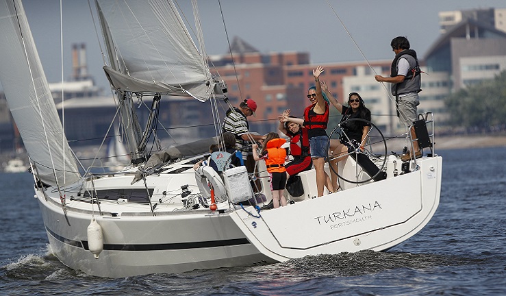 A group of people are waving and smiling onboard a yacht